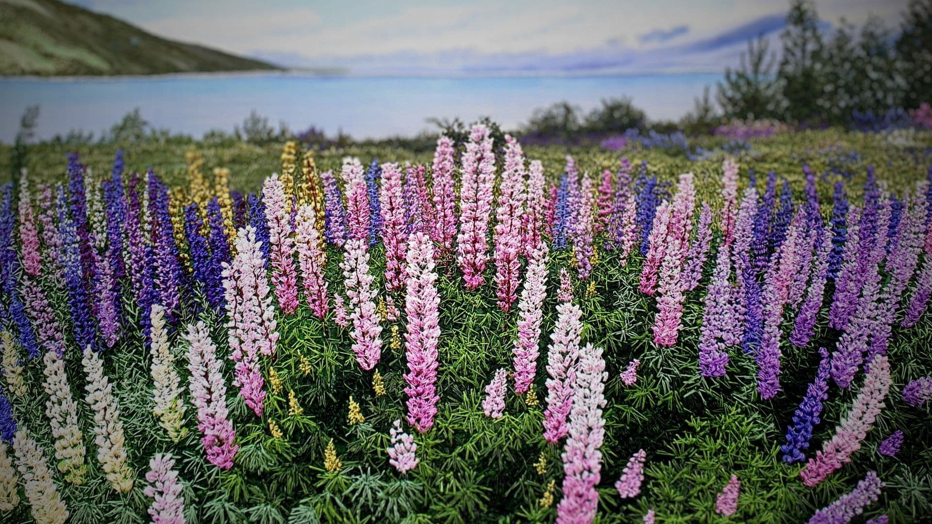 A machine embroidered field of lavender and flowers in the foreground and the sea beyond